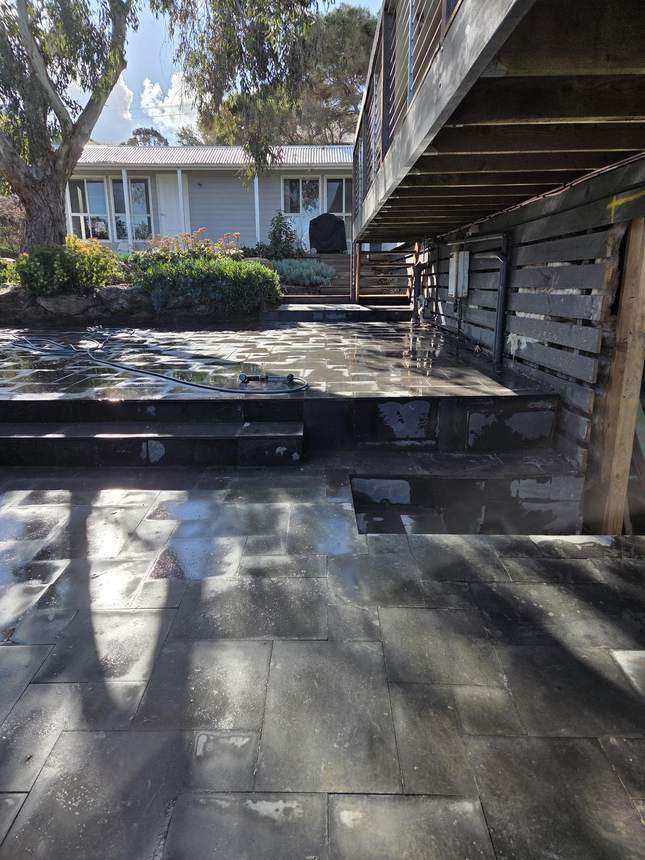Bluestone wall face from the side with deck structure above and drainage channel at base