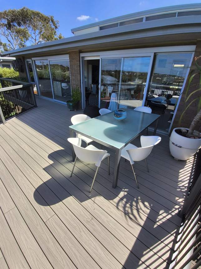Looking down the full length of the finished composite deck with outdoor furniture at far end — Jan Juc