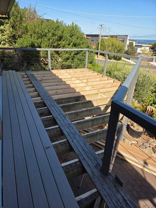 Old deck boards lifted exposing the joists and frame, first new boards started — Jan Juc