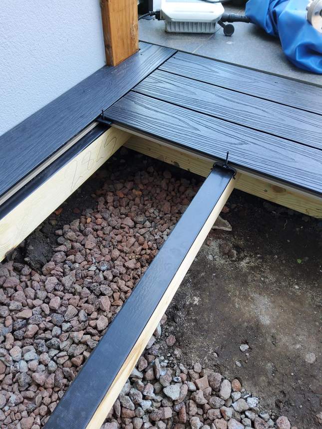 Dark charcoal composite deck boards being clipped — concealed fixings, drainage visible below — Pakenham