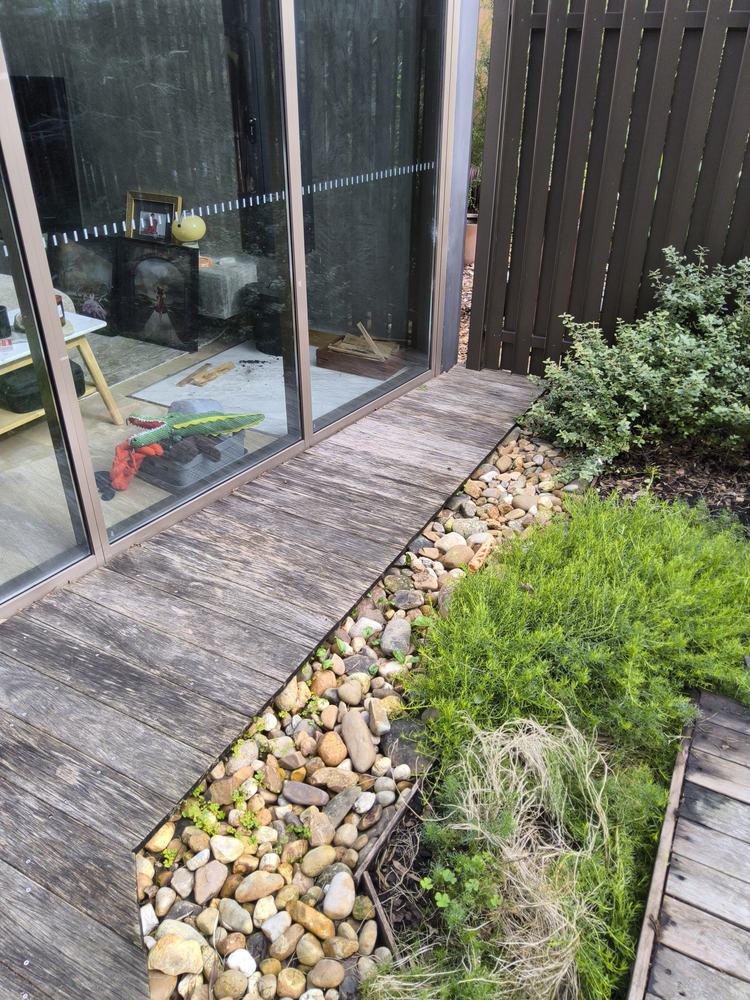 Narrow timber deck strip beside the glass with river-stone channel